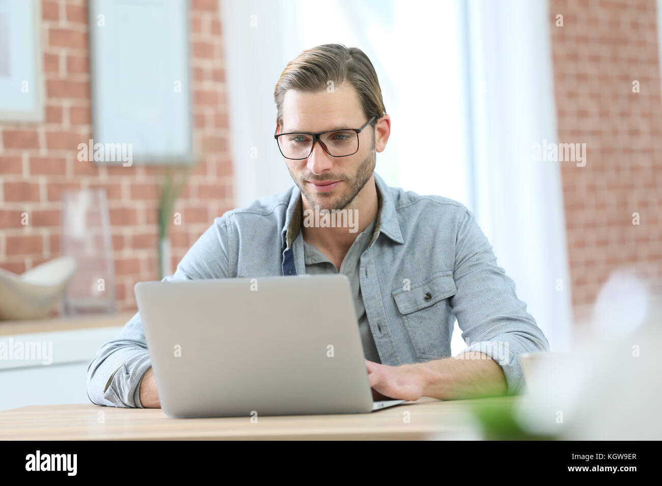 Blond guy with eyeglasses sitting in front of laptop computer at home ...