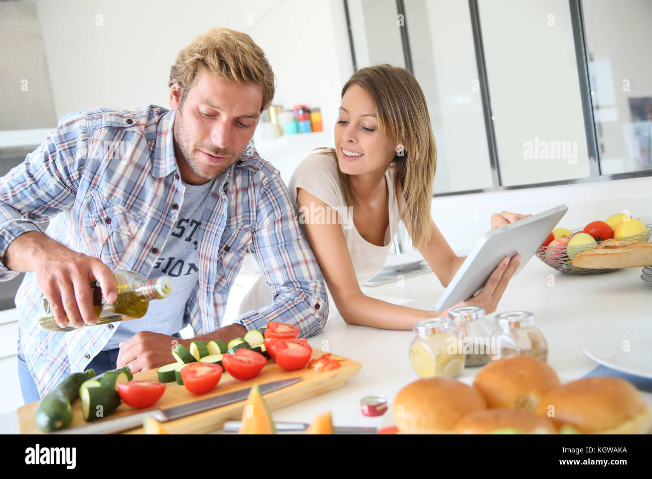 Cheerful couple in kitchen cooking dinner, using tablet Stock Photo