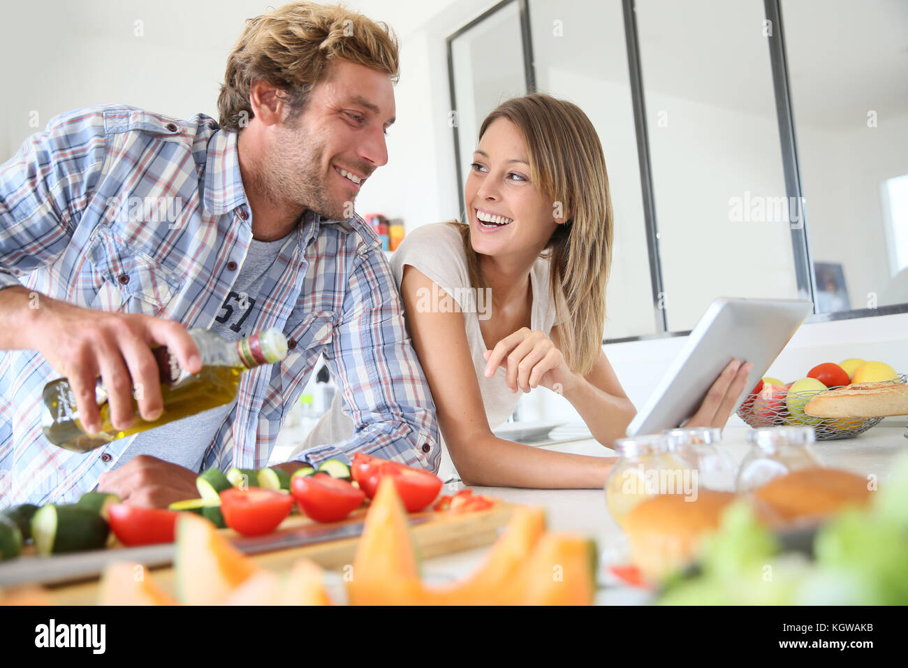 Cheerful couple in kitchen cooking dinner, using tablet Stock Photo