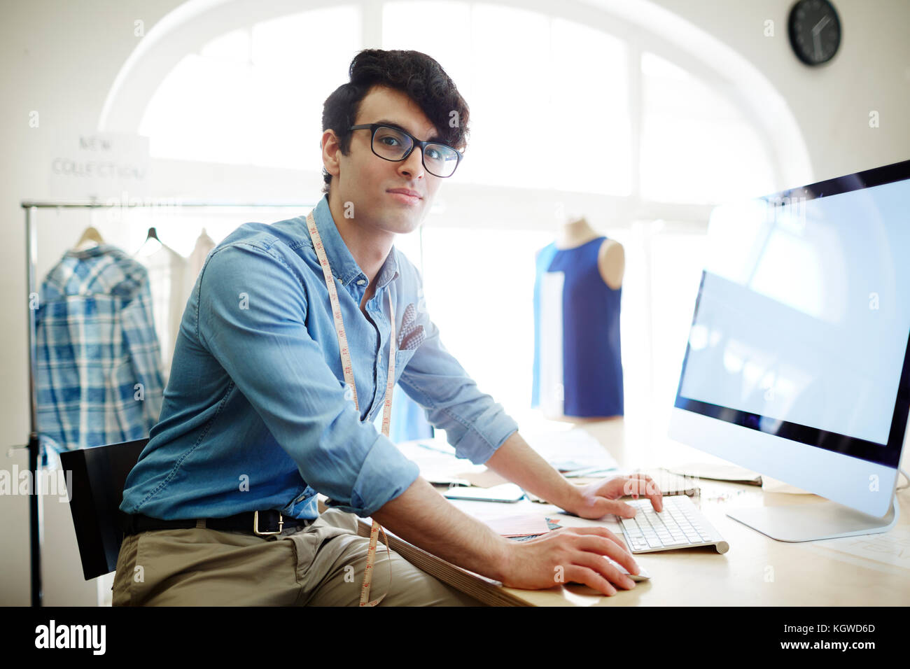Young creative fashion designer sitting by workplace in front of
