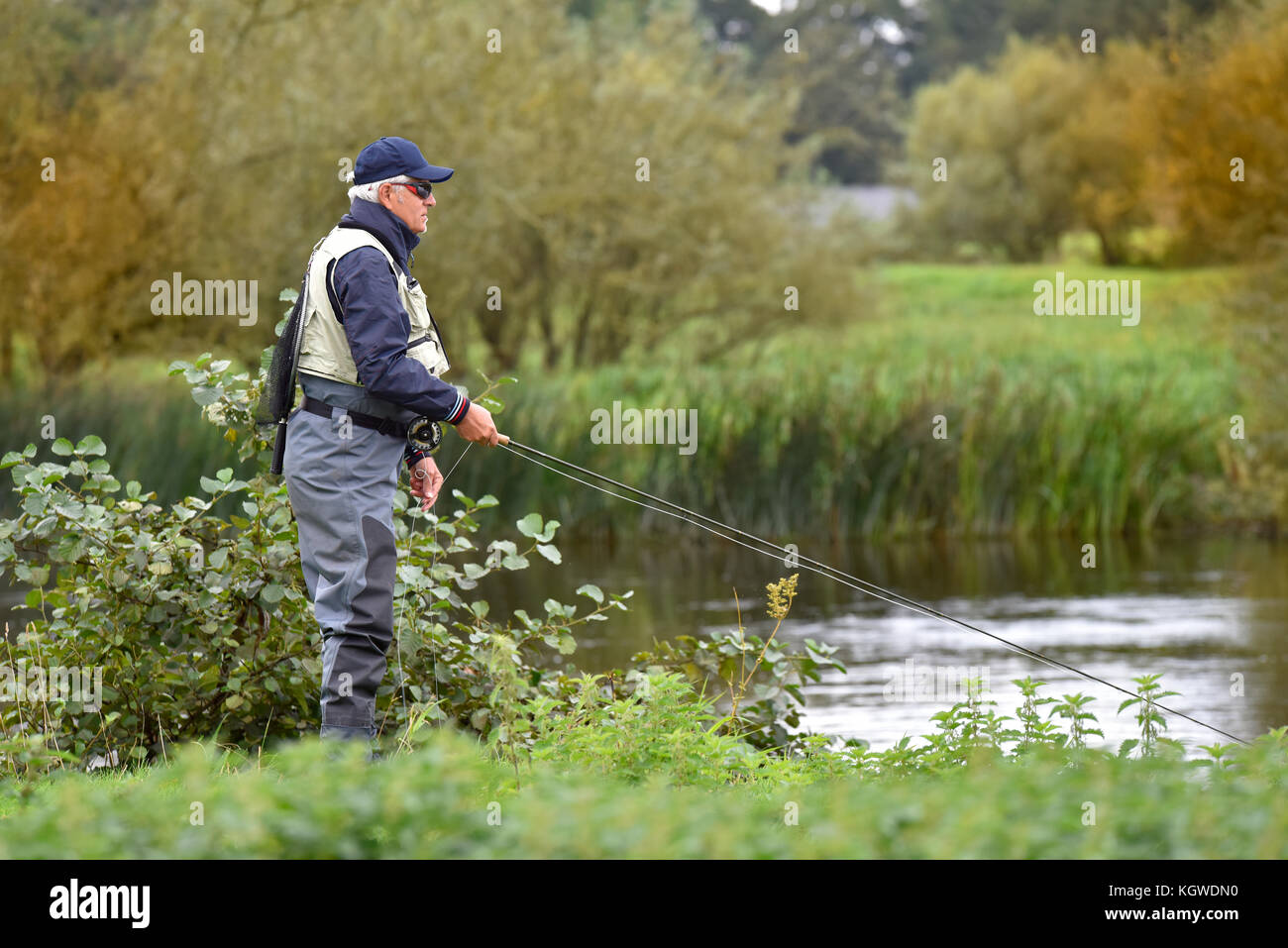 Fly-fisherman fishing in river from riverbanks Stock Photo