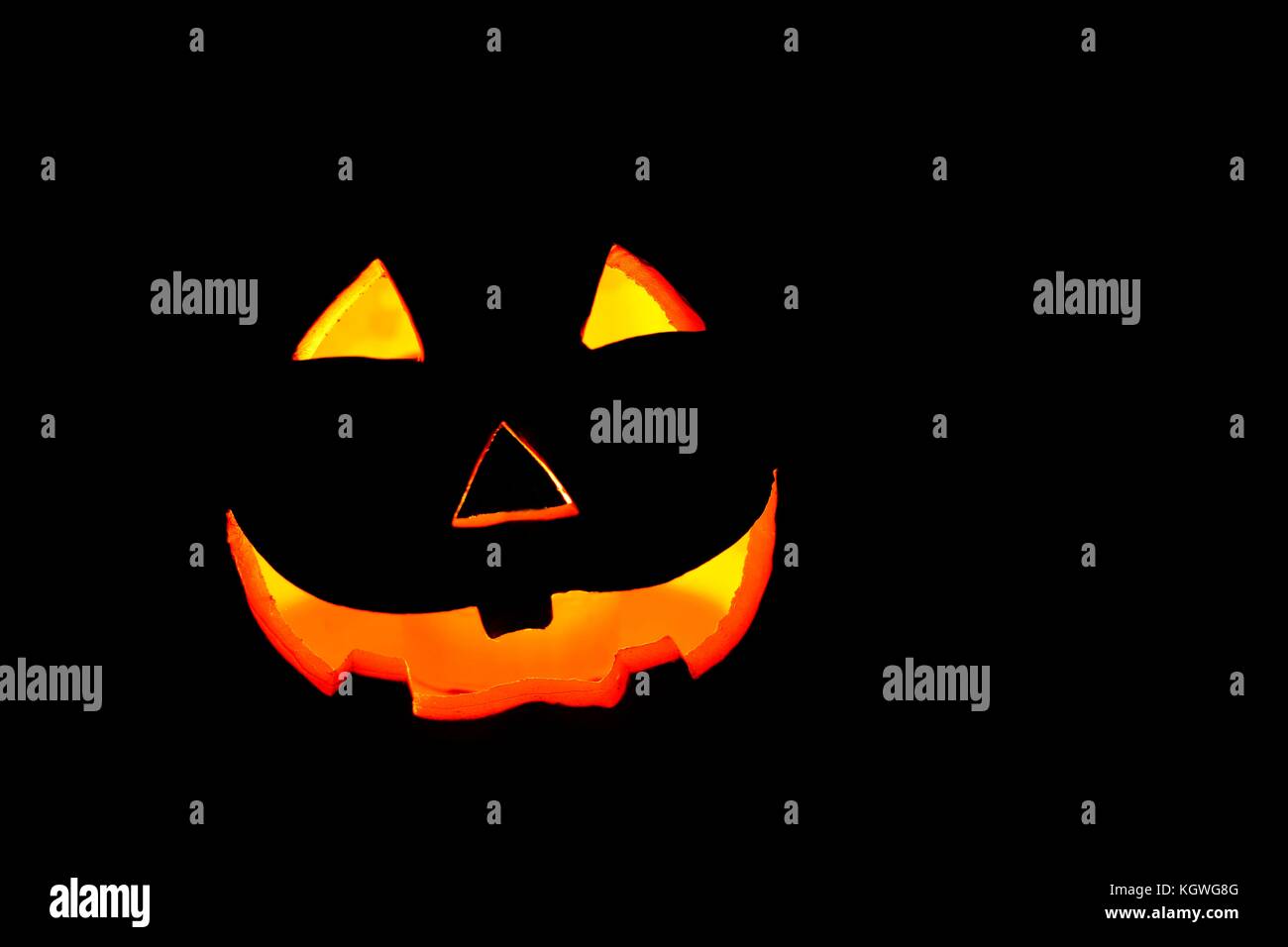 Illuminated Halloween smiling spooky pumpkin face on a dark background ...