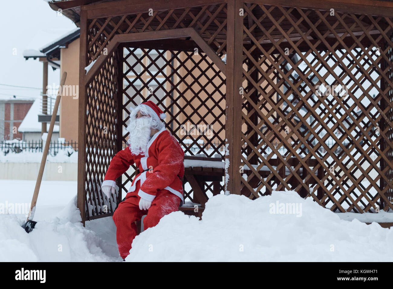Tired santa claus sitting on wooden chair after work of snow removal in front of wooden house Stock Photo