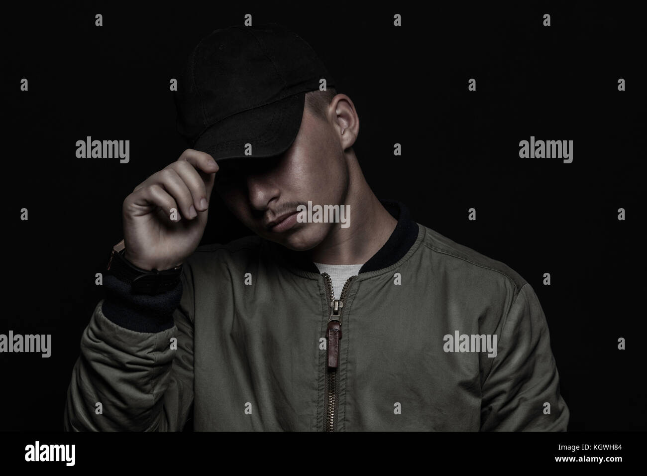 teen boy holding cap with bomber jacket in front of black background Stock Photo