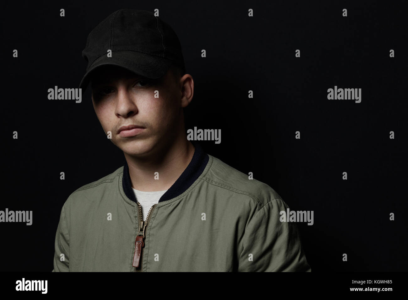 teen boy posing with black cap and bomber jacket in front of black background Stock Photo