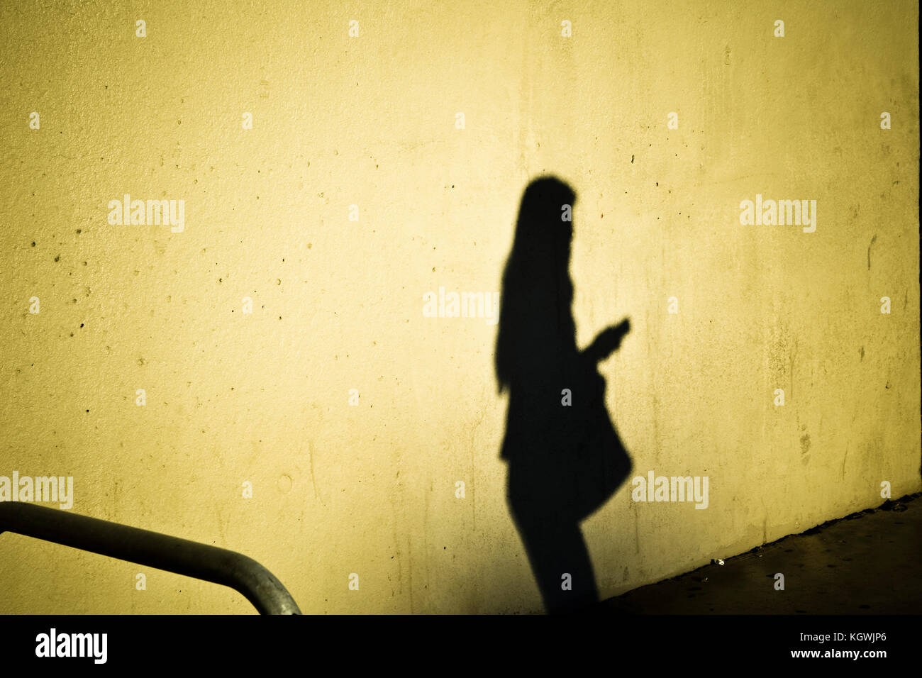 Silhouette of woman holding mobile, shadow on a wall. Stock Photo