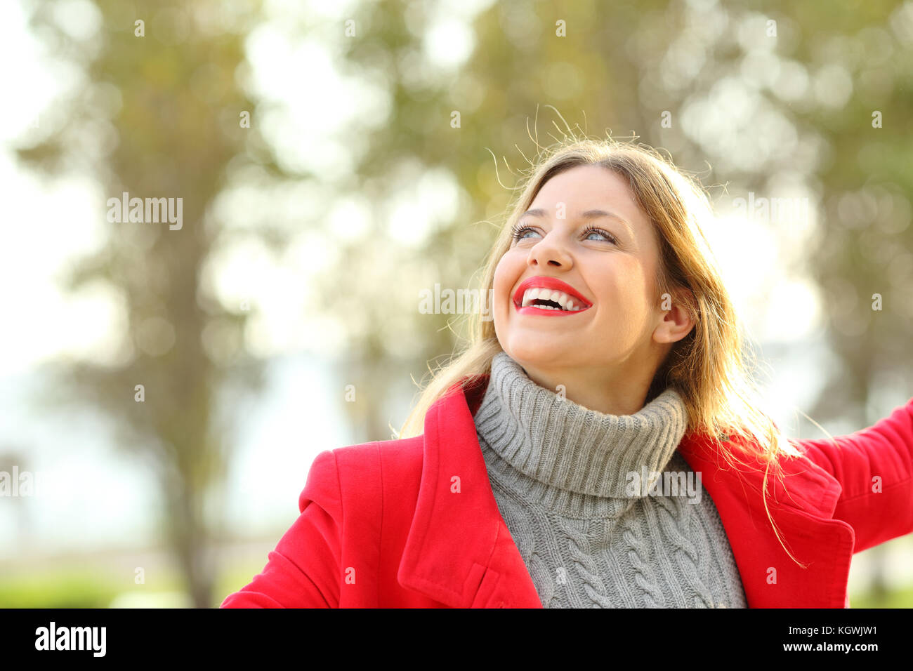 Portrait of a joyful candid girl wearing a red jacket and a sweater joking outdoors in a park in winter Stock Photo
