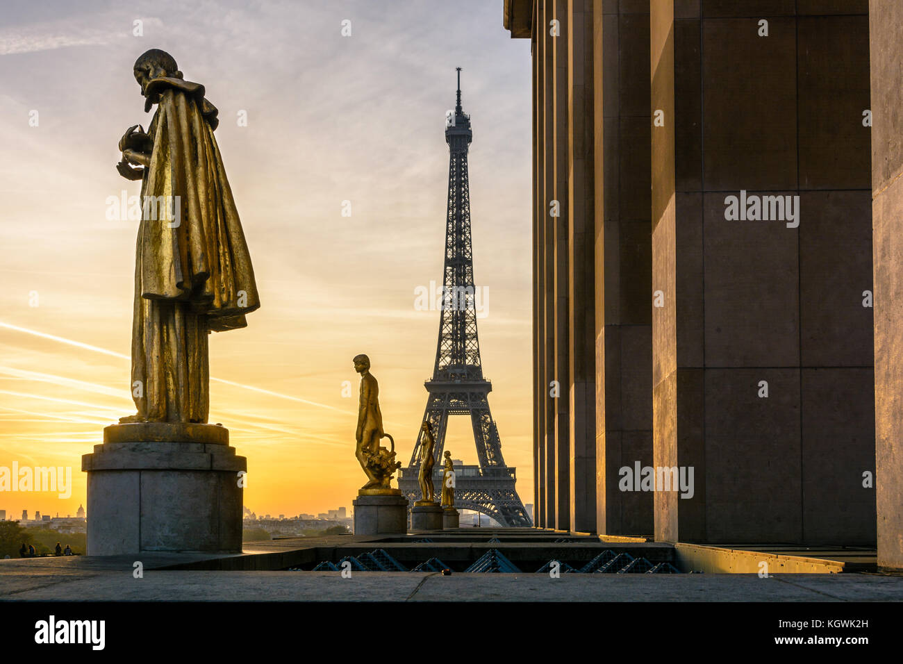The rising sun illuminates the golden statues on the Trocadero esplanade while the Eiffel Tower stands out against an orange sky. Stock Photo