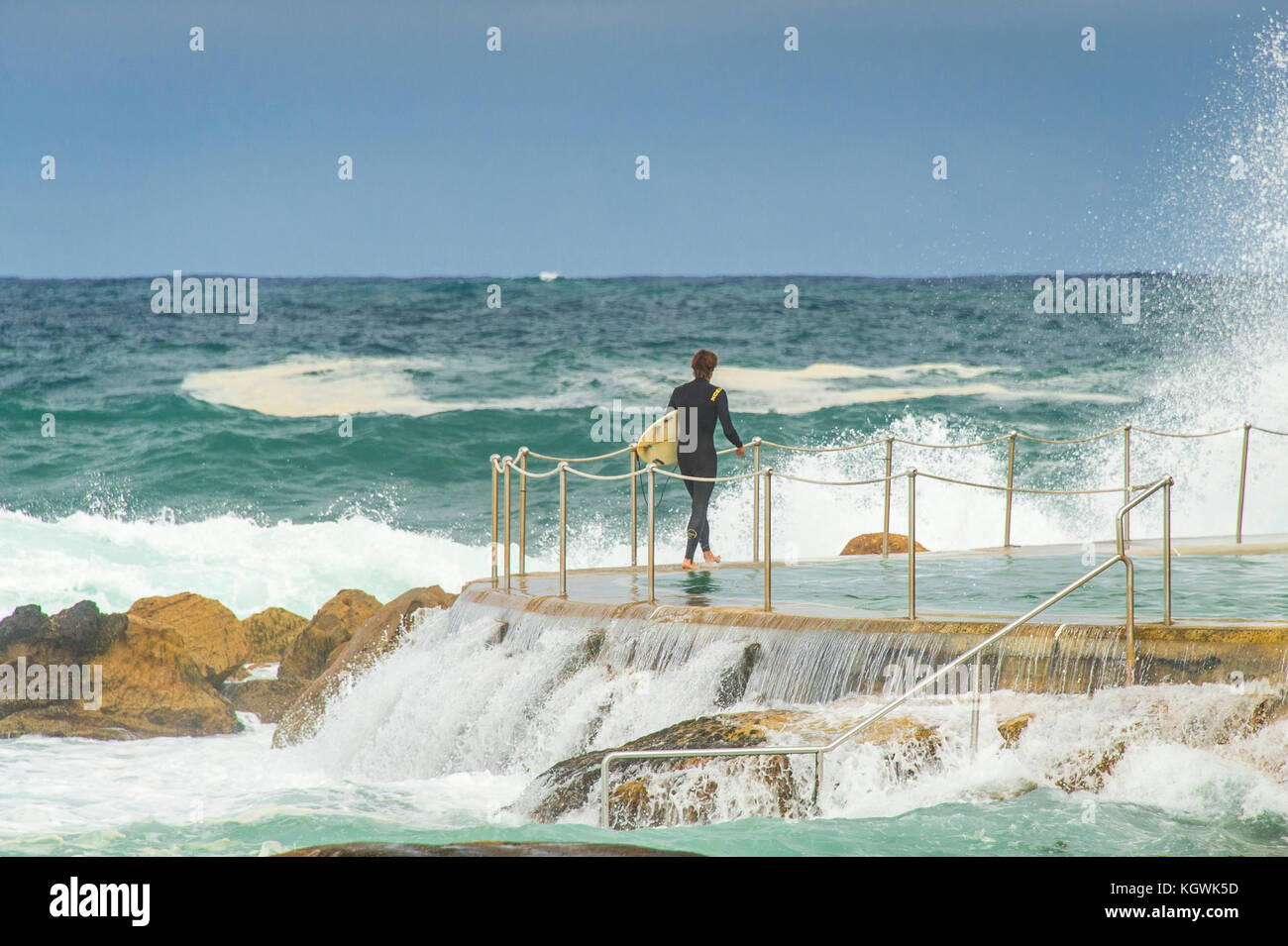 A male surfer waits for the right time to enter the water from the Bronte Beach rock pool in Sydney, NSW, Australia in big surf conditions Stock Photo