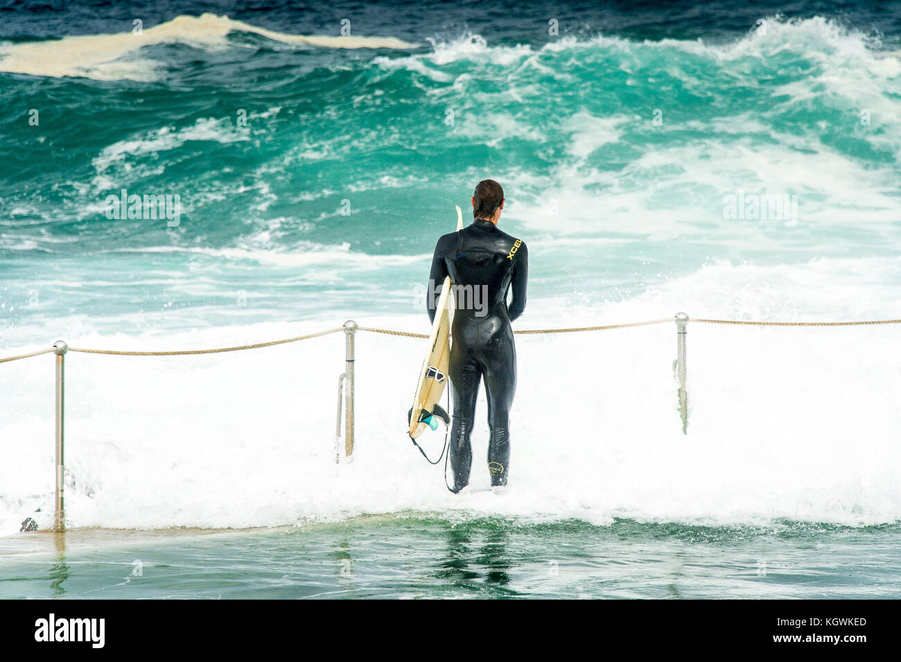 A male surfer waits for the right time to enter the water from the Bronte Beach rock pool in Sydney, NSW, Australia in big surf conditions Stock Photo