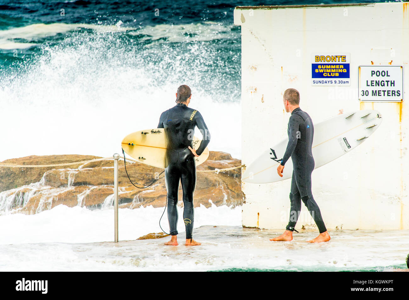 Two surfers wait for the right time to enter the water from the Bronte Beach rock pool in Sydney, NSW, Australia in big surf conditions Stock Photo