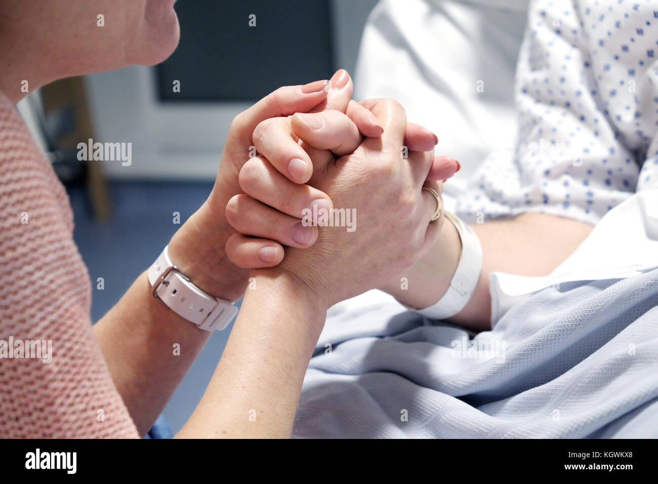 A mother clasps the hand of her son who is lying ill in a hospital bed. Offering support as he starts his recovery, Taken in Bristol, UK Stock Photo