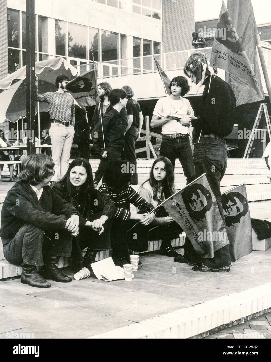 Students dressed in hippie attire sit on the steps of a campus building holding flags with the exhiled guerilla leader Che Guevara, part of a student sit-in protest against the Vietnam War and United States action in Cambodia, at North Carola State University, Raleigh, North Carolina, 1970. Stock Photo