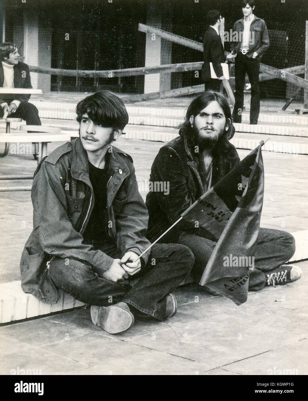 Two male students wearing hippie attire sit on a step, with one holding a flag with the face of revolutionary Che Guevara, during an anti Vietnam War student sit-in protest at North Carolina State University, Raleigh, North Carolina, 1970. () Stock Photo