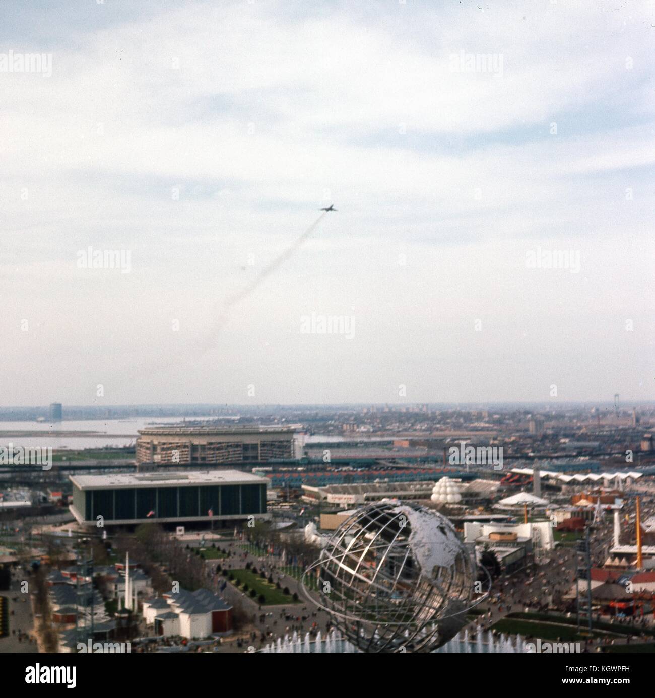 Panoramic aerial view facing north-northwest taken from the New York State Pavilion observation tower at the New York World's Fair, Flushing Meadows-Corona, Queens, New York, May, 1965. An airplane with contrails flies off from LaGuardia Airport at center frame. Seen below are the major landmarks of the fair: the steel globe Unisphere in the foreground, the United States Pavilion building at lower left, and the William A. Shea Municipal Stadium directly behind at midground. In the background is the neighborhood of College Point on the shoreline of Flushing Bay. Stock Photo