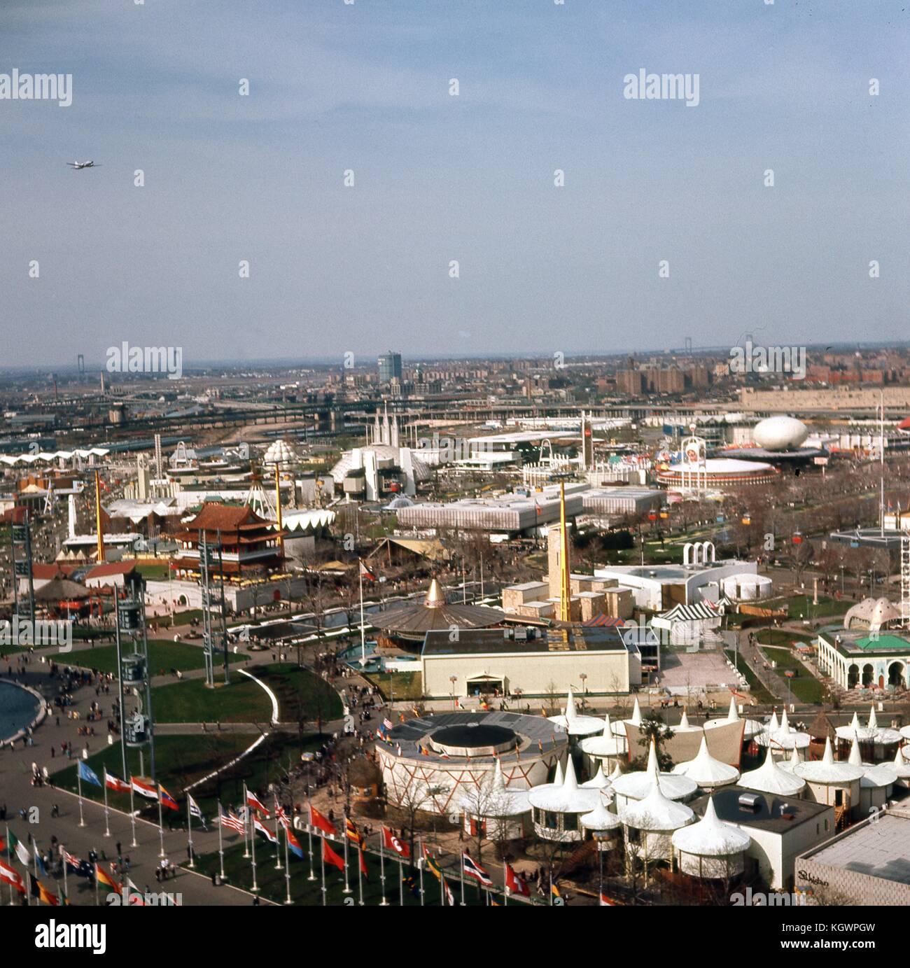 Panoramic view facing northeast of the New York World's Fair, taken from the observation tower at the New York State Pavilion, in Flushing Meadows-Corona, Queens, New York, May, 1965. At upper left corner is an airplane taking off from LaGuardia Airport along Flushing Bay. The Whitestone and Throgs Neck Bridges spanning the Long Island Sound are seen from left to right in the extreme distance. In the midground are a multitude of fair exhibits located on either side of the Promenade: the Spain Pavilion; the 7-Up and Dupont exhibits next to the famed IBM egg; the national pavilions of the Philip Stock Photo