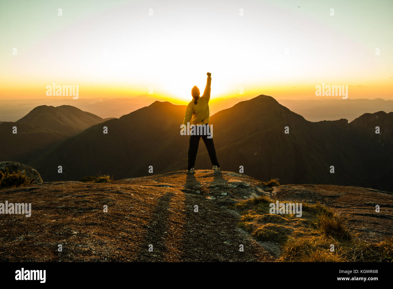 Man celebrating success on top of a mountain with one arm Raised and Hands Closed Stock Photo