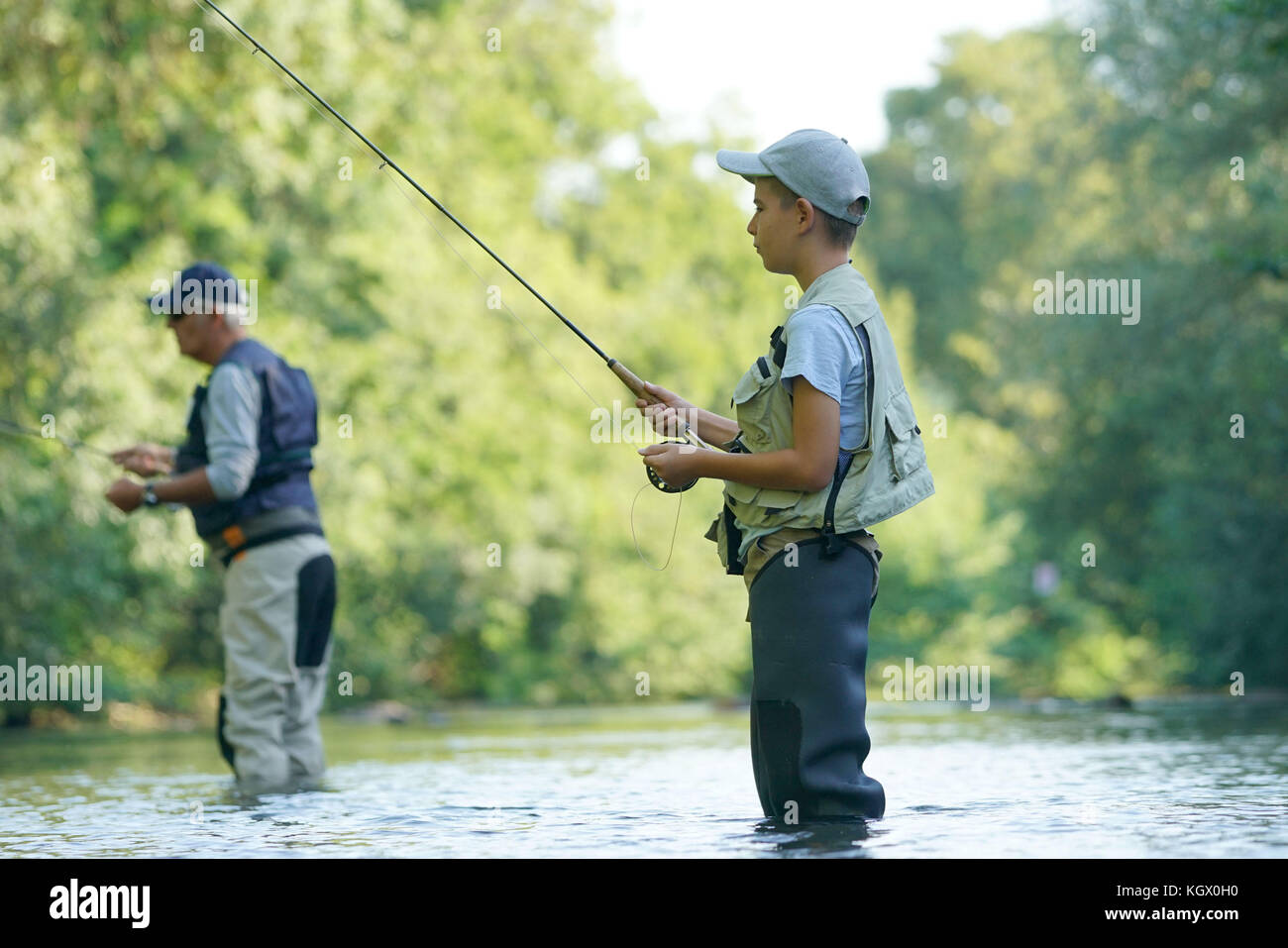 Young boy fly fishing in river, dad in background Stock Photo