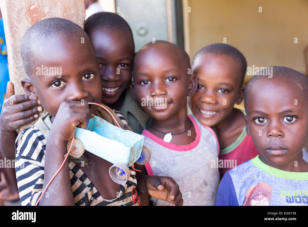 A bunch of children laughing, waving and having fun posing in front of the camera. One of them is holding a simple toy car made out of a bottle and bo Stock Photo