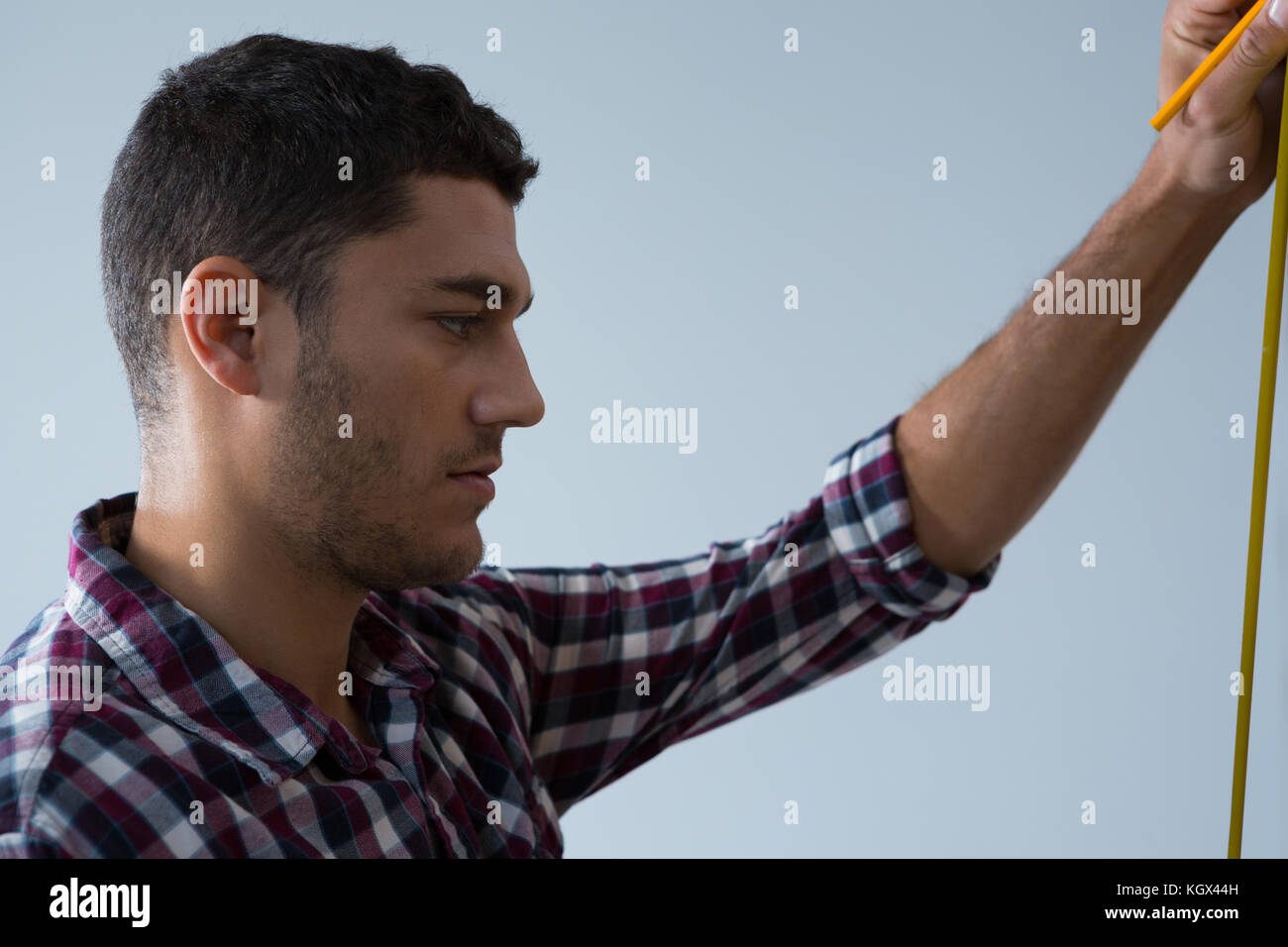 Side view of male architect measuring wall with measuring tape Stock