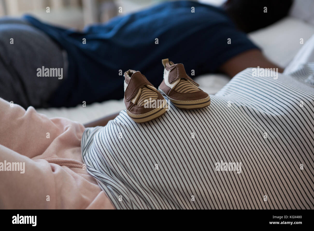 Pregnant woman relaxing with baby shoes on her belly in bedroom at home Stock Photo
