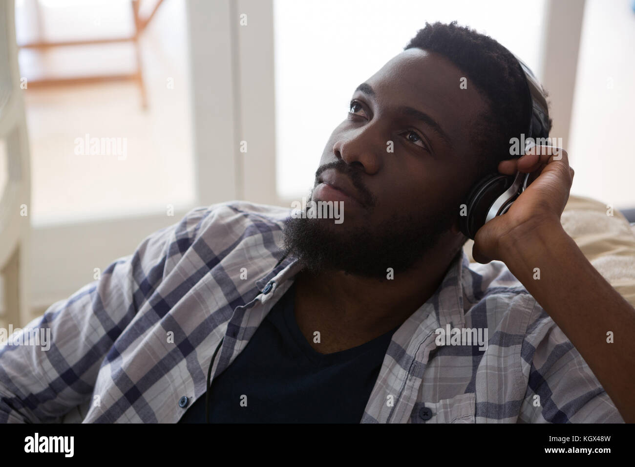 Thoughtful man listening to music on headphones at home Stock Photo