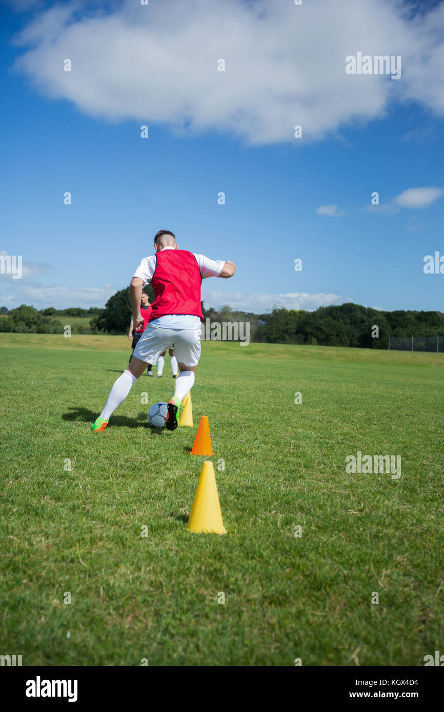 Soccer player dribbling through cones in the ground on a sunny day