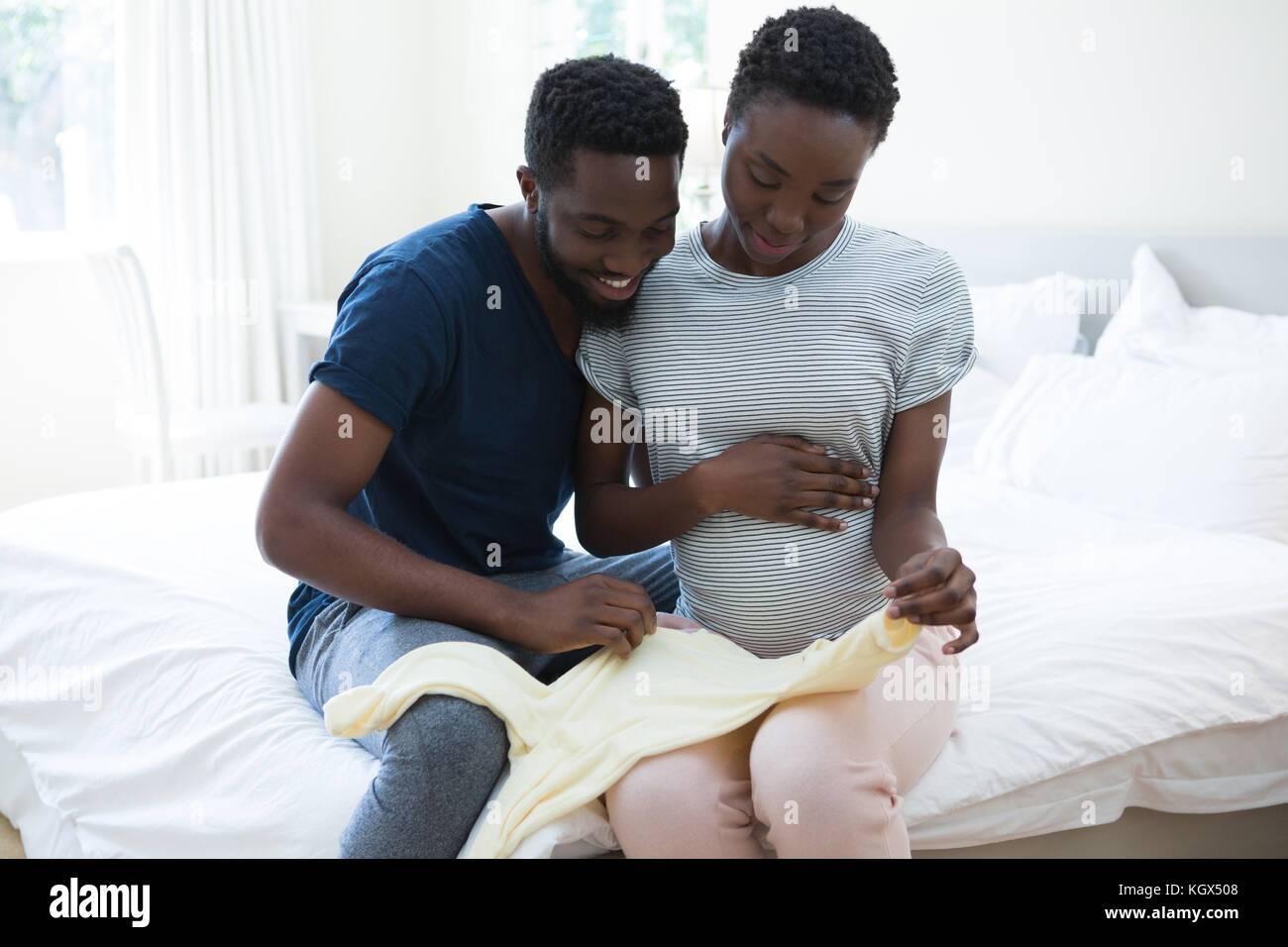 Happy couple holding baby clothes in bedroom at home Stock Photo
