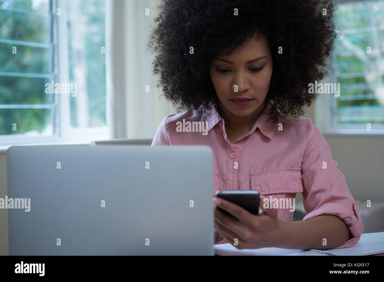 Woman using mobile phone while working at desk in home Stock Photo - Alamy