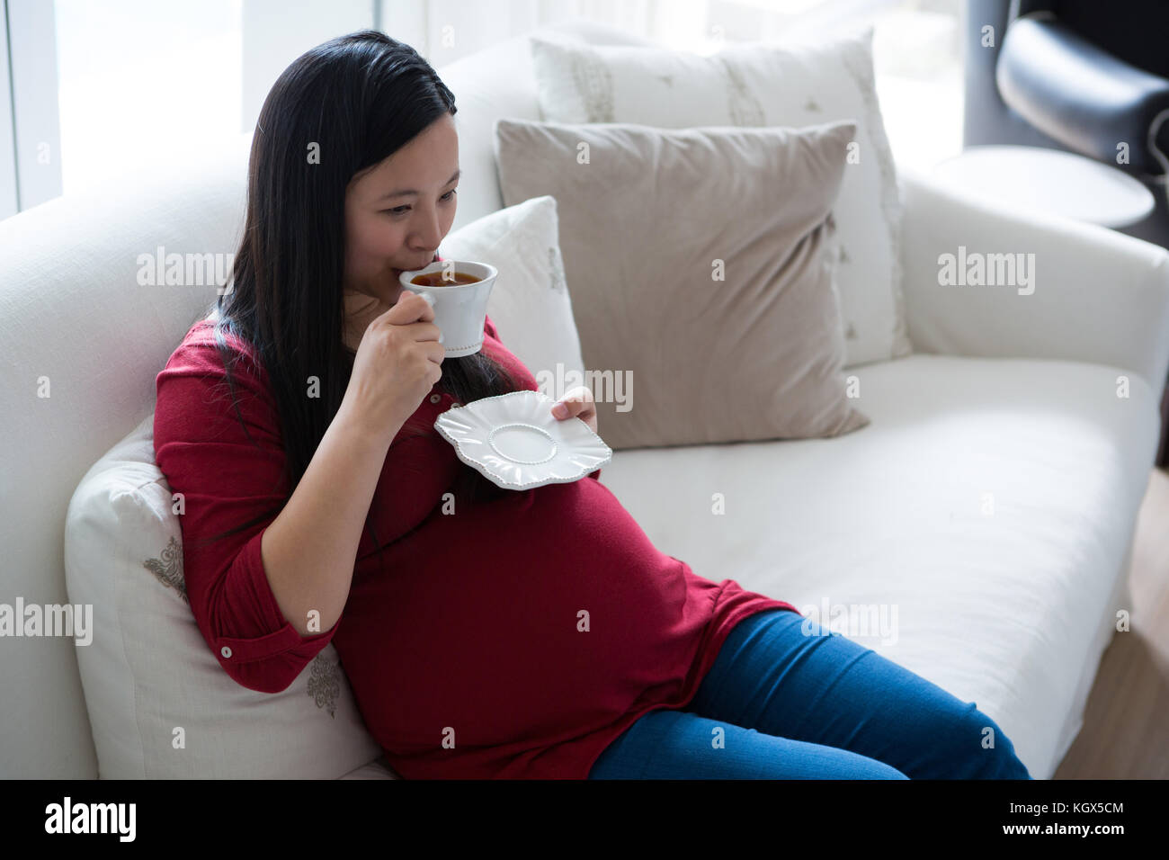 Pregnant woman having coffee in living room at home Stock Photo