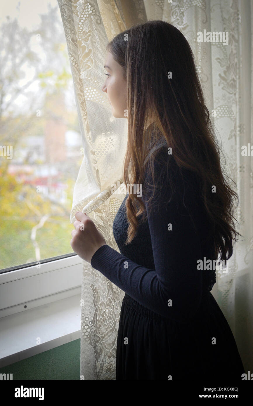 Young girl in black vintage dress standing near window Stock Photo