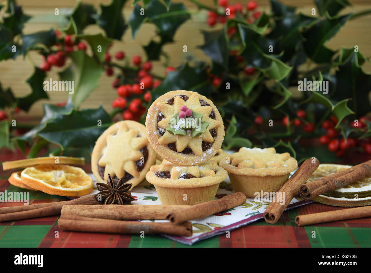 Christmas food photography image with traditional iced pastry fruit mince pies and star top with real fresh green holly and red berries in background Stock Photo