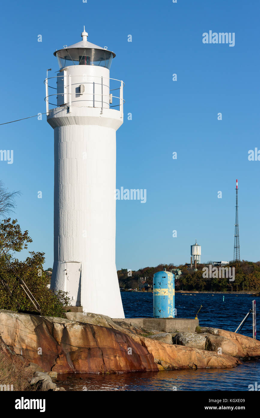 Small white lighthouse on the Karlskrona (Sweden) archipelago island of Stumholmen with coastal landscape in background. Water tower and radio antenna Stock Photo