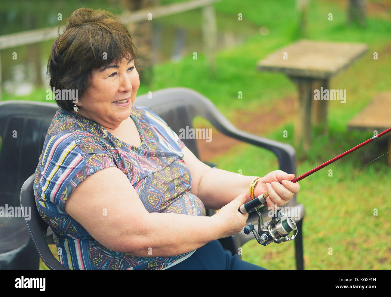 Old woman seated, smiling, fishing, holding a fishing rod. Brazilian women descendant of japanese fishing. Stock Photo