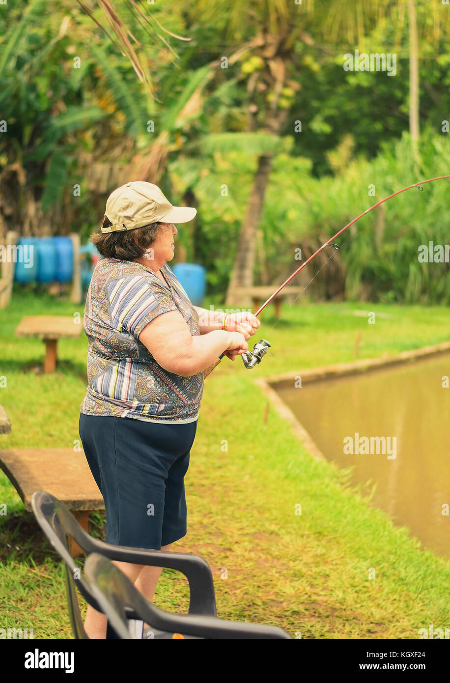 Old woman holding a fishing rod, hooking a fish on a lake. Brazilian women descendant of japanese fishing. Stock Photo