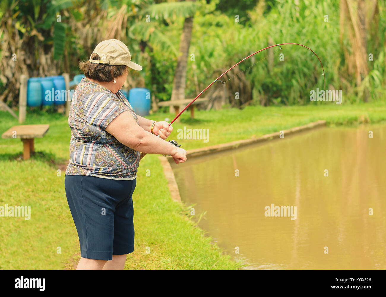 Old woman holding a fishing rod, hooking a fish on a lake. Brazilian women descendant of japanese fishing. Stock Photo