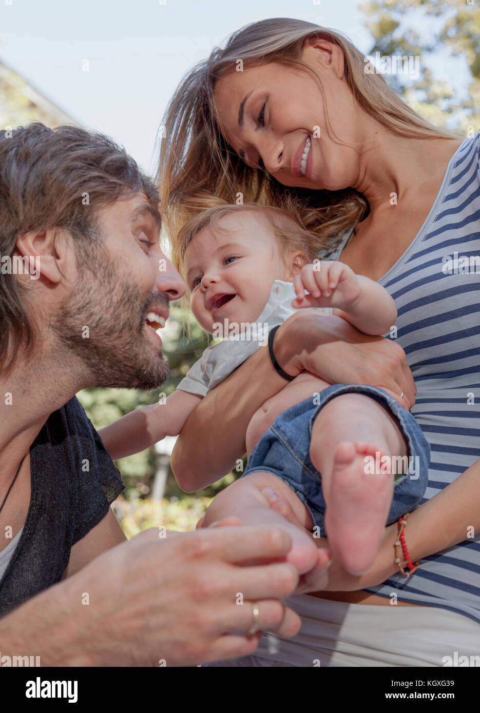 A young beautiful couple are teesing their happy woughing cute baby. Stock Photo