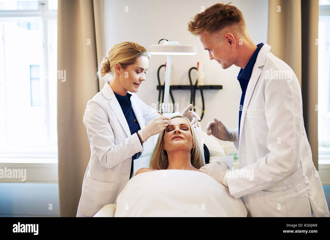 Two young doctors discussing a cosmetic surgery treatment on the face of a  mature woman lying on a table in a clinic Stock Photo - Alamy