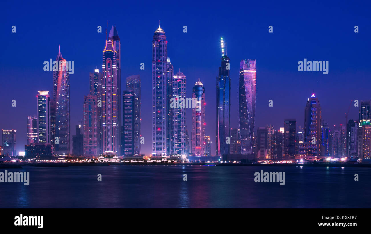 Wide view of Dubai skyline on the waterfront during the blue hour, with modern buildings and skyscrapers lit up. February 2016. Stock Photo