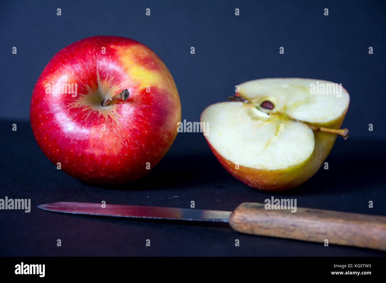 Whole, red, ripe, tasty apple with a knife, half of and apple on black background Stock Photo