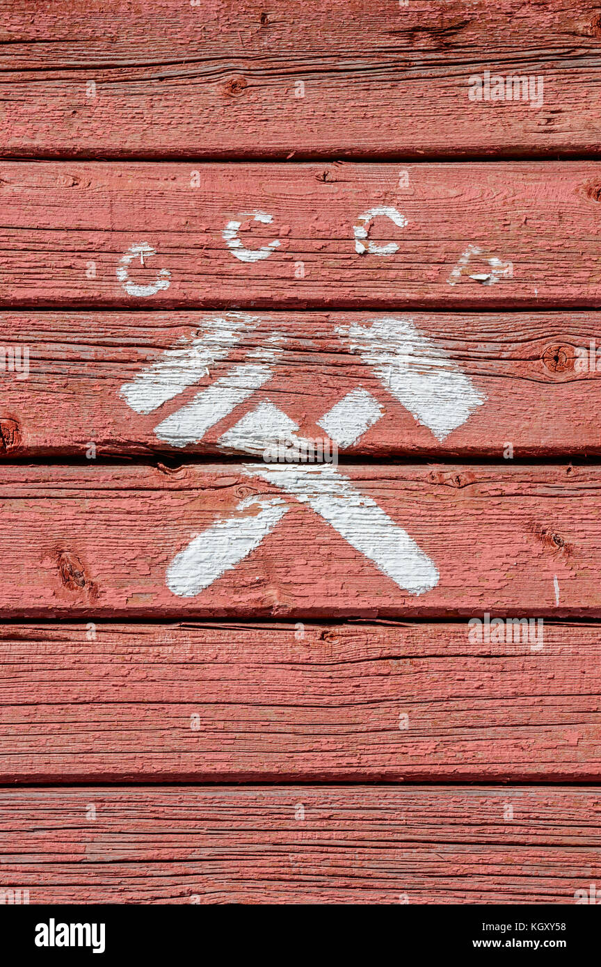 Letters CCCP (russian abbr. for USSR) and a crossed hammer and monkey wrench, a communist symbol, painted in white on a red, weathered, wooden surface Stock Photo