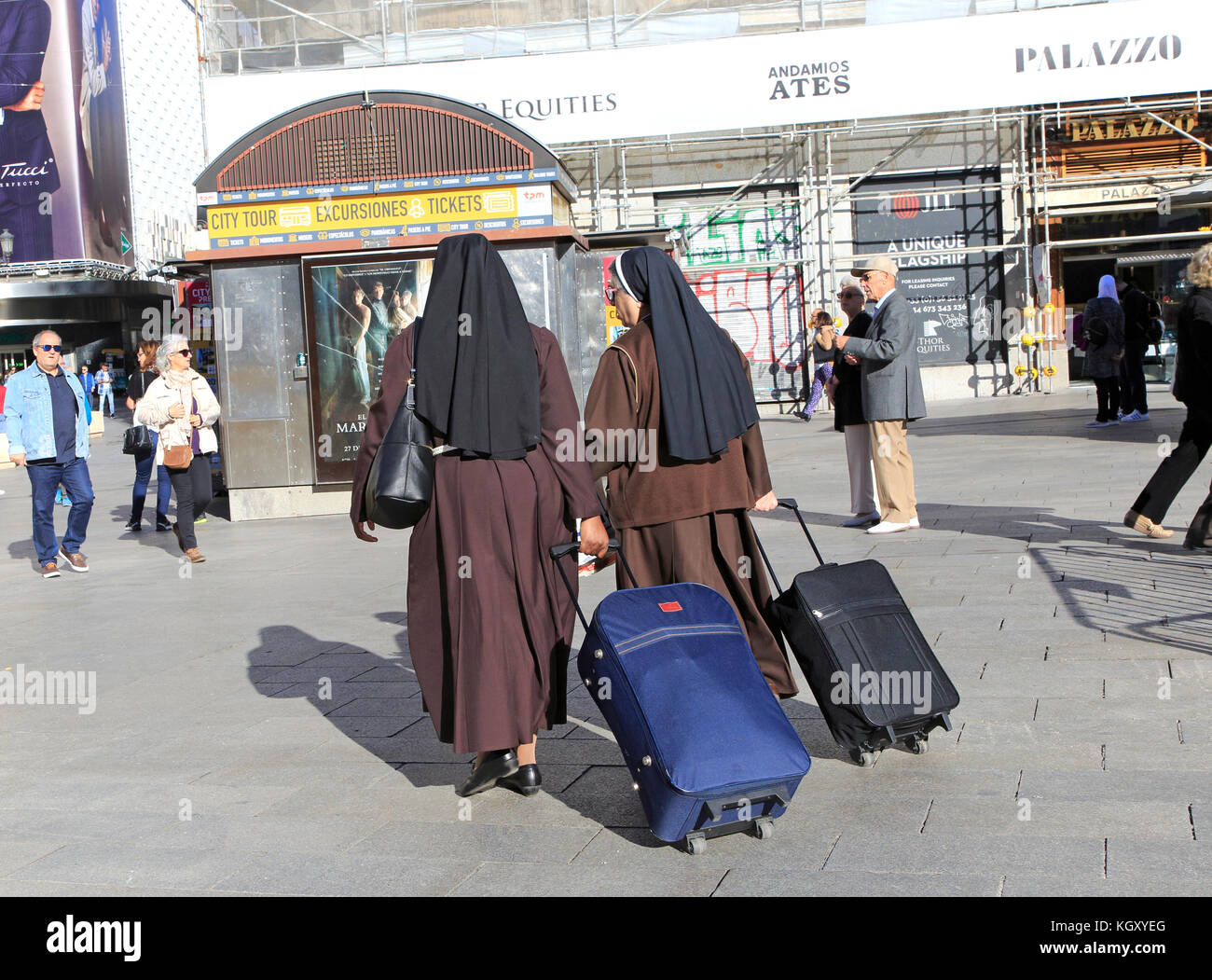 Two nuns wearing brown habits each pulling a suitcase in Madrid city centre, Spain Stock Photo