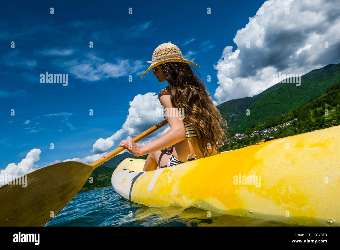 Young woman with long hair and hat kayaking in sun on lake Stock Photo