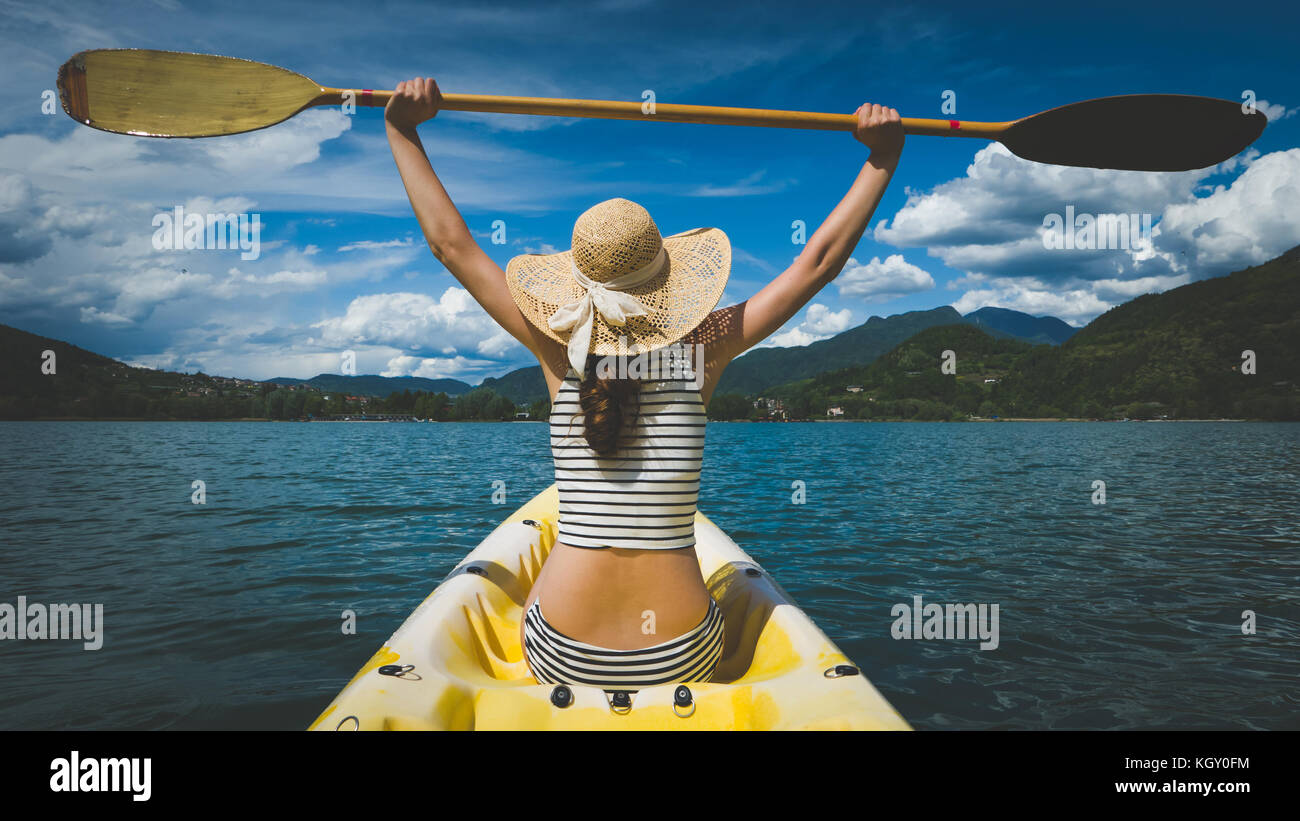 Young woman with long hair and hat kayaking in sun on lake Stock Photo