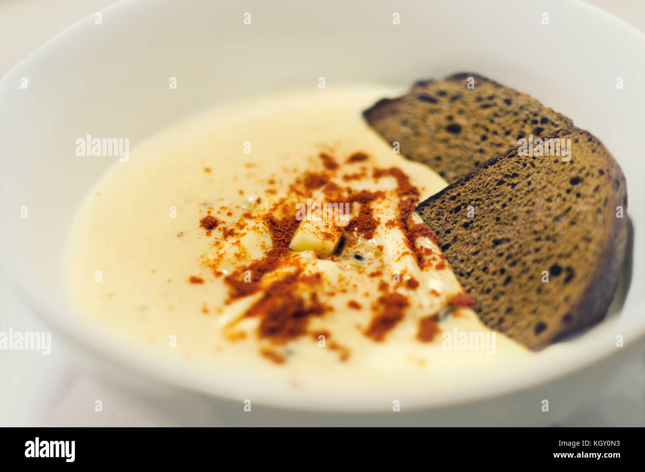 Cream soup sprinkled with paprika with rye bread in a white plate. Photo with shallow depth of field. Stock Photo