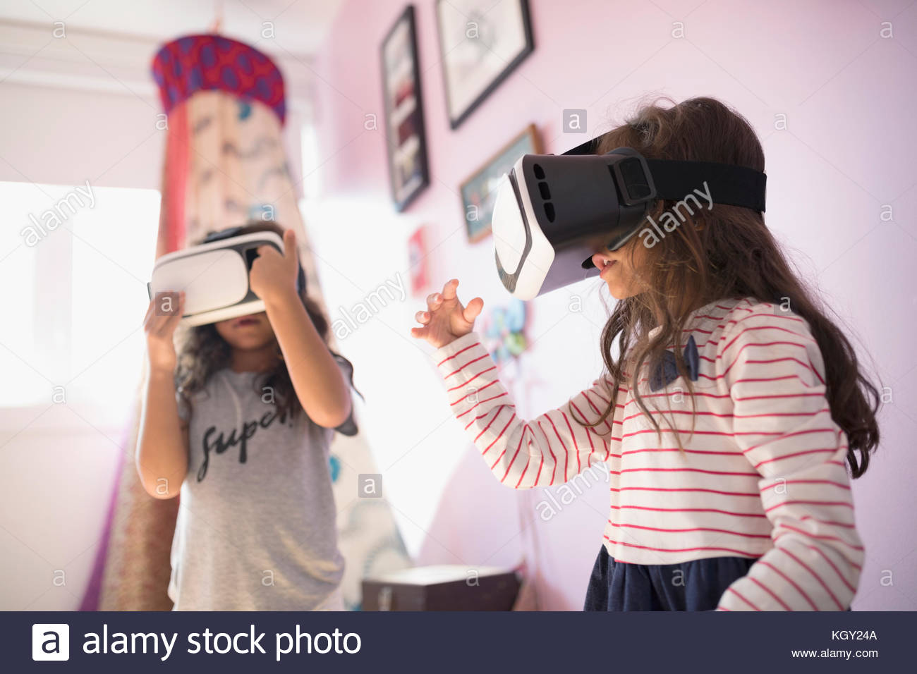Girl sisters playing with virtual reality simulator glasses in bedroom Stock Photo