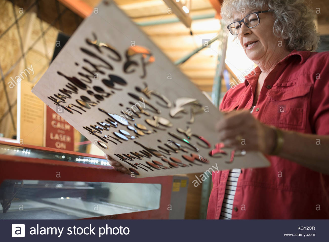 Senior female machinist examining laser cut wood sign at laser cutter in workshop Stock Photo