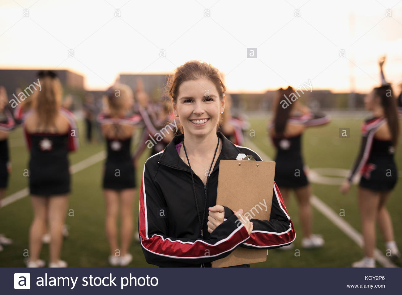 Portrait smiling, confident high school cheerleading coach with clipboard on sideline of