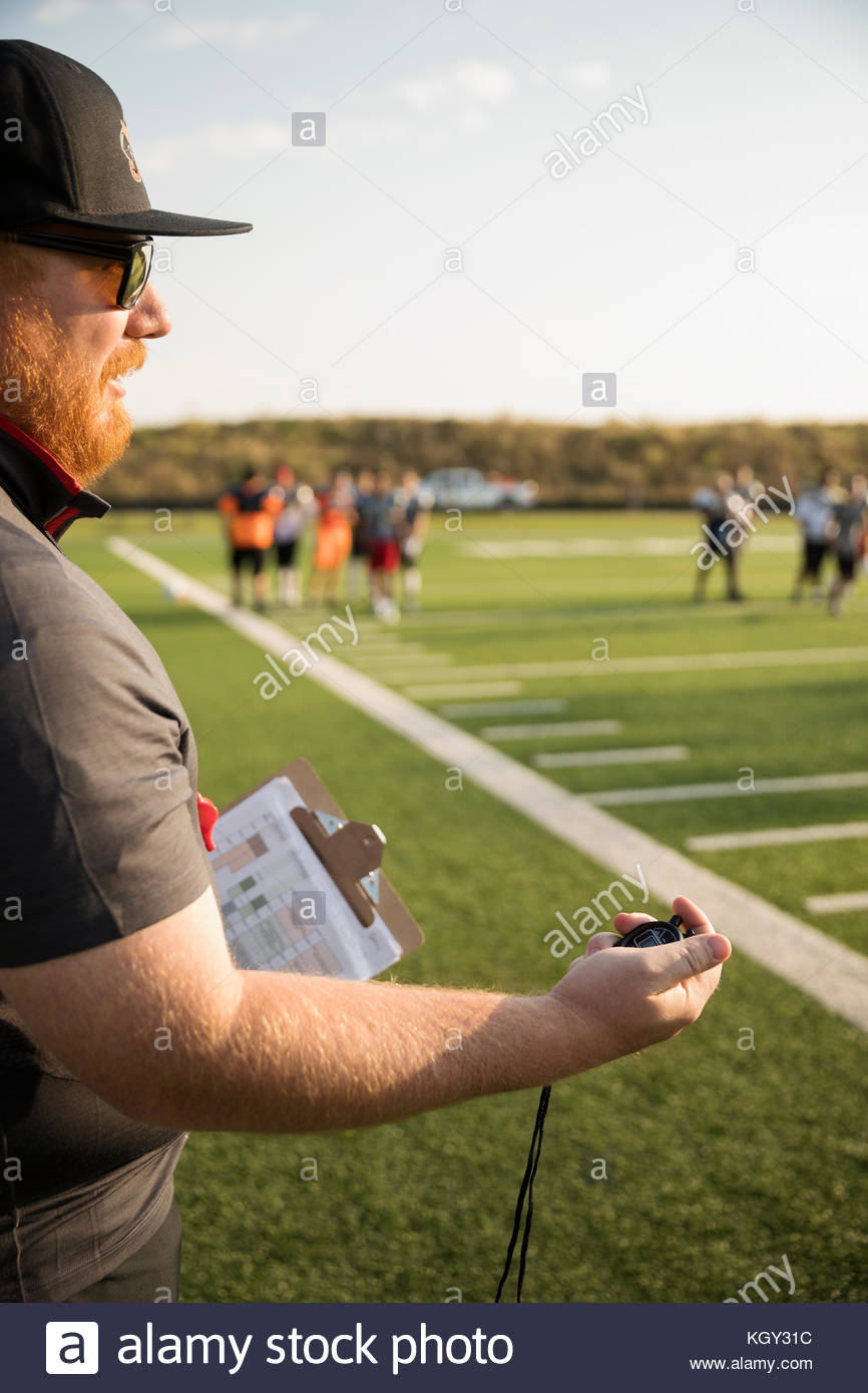 High school football coach with stopwatch timing practice on football