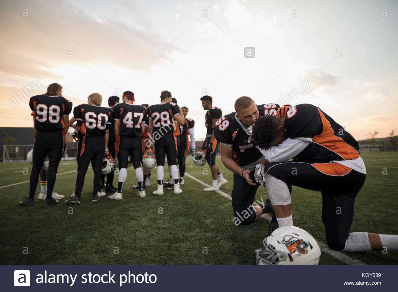 Teenage boy high school football player consoling teammate on football field Stock Photo